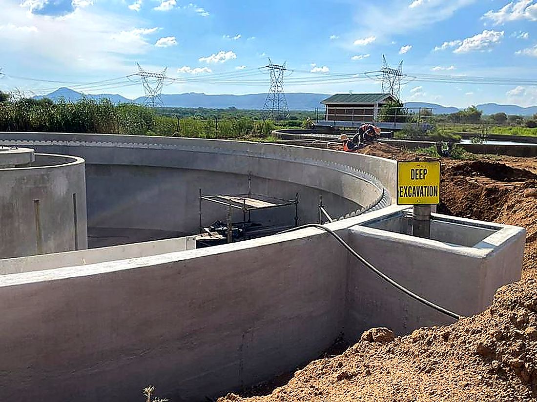Circular reinforced concrete reservoir under construction with mountains beyond